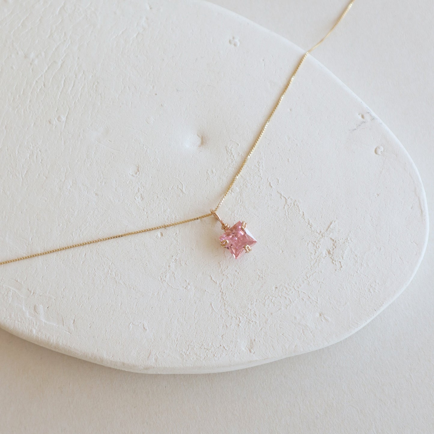 Gold necklace with a pink gemstone on a white stone surface