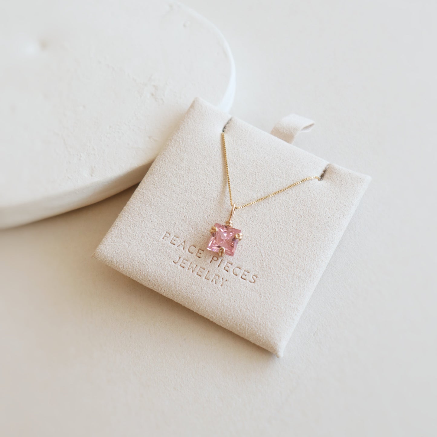 Gold necklace with a pink pendant on a branded jewelry pouch against a light background