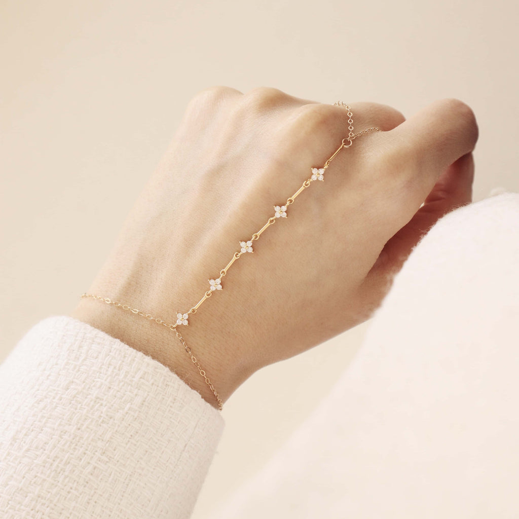 Hand wearing a delicate gold bracelet with star-shaped charms on a neutral background