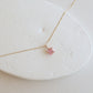 Gold necklace with a pink gemstone on a white stone surface