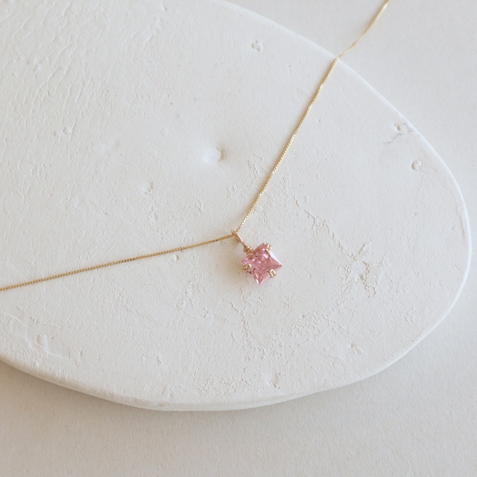 Gold necklace with a pink gemstone on a white stone surface