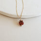 Gold necklace with a red gemstone pendant on a light background