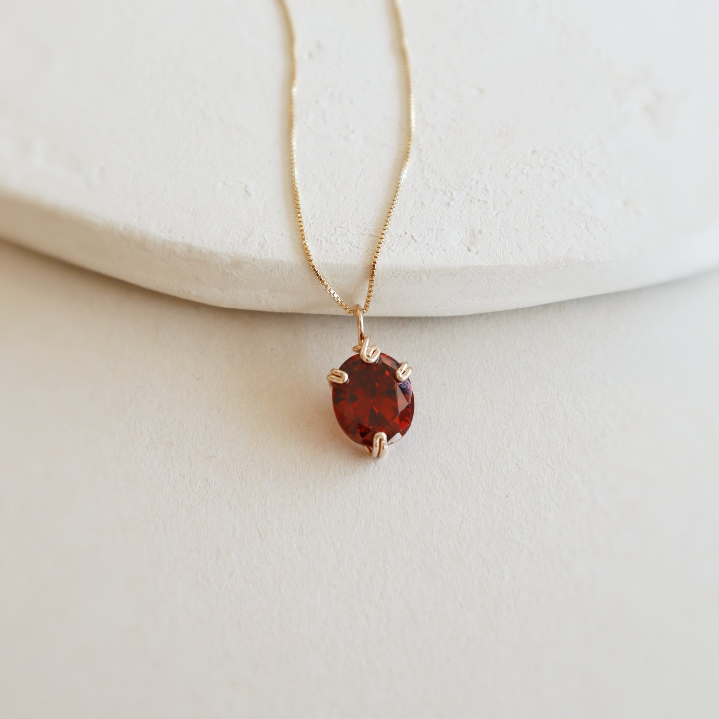 Gold necklace with a red gemstone pendant on a light background