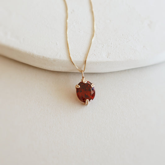 Gold necklace with a red gemstone pendant on a light background